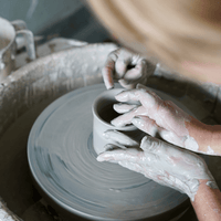 Brudne od gliny dłonie toczące kubek na kole garncarskim w czasie warsztatów ceramicznych